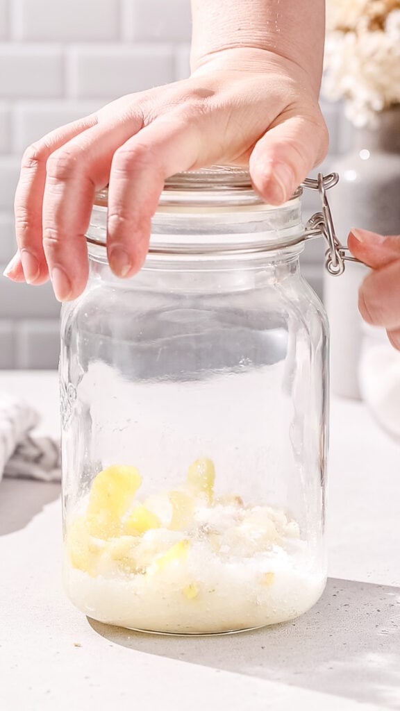 Hand sealing up a glass jar filled with the sugar, lemon and ginger.