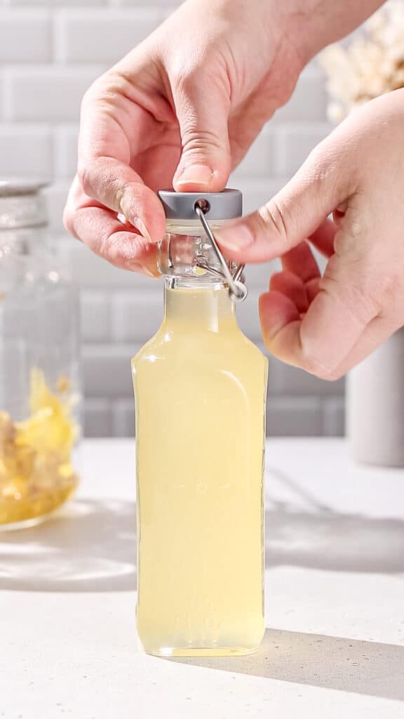Hands sealing a swing-top bottle with the ginger shrub inside.