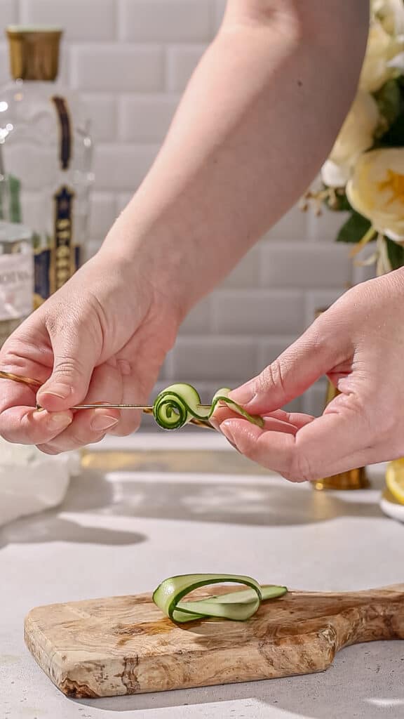 Hands adding a cucumber ribbon to a cocktail pick.