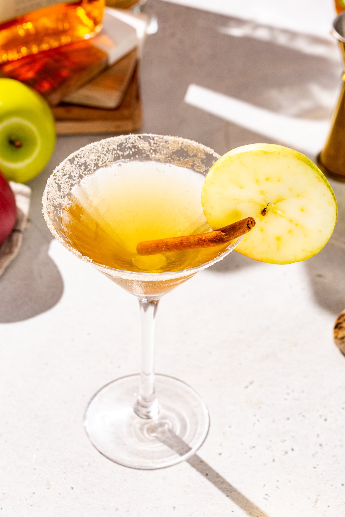 Overhead view of an Apple cider martini on a countertop. The drink has a cinnamon sugar rim, a cinnamon stick and an apple slice garnish.