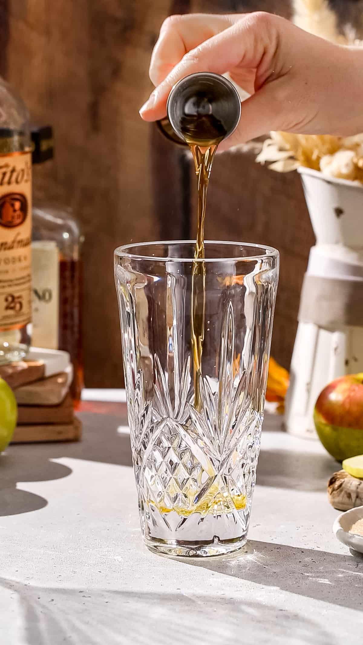 Hand pouring amaretto into a cocktail shaker.