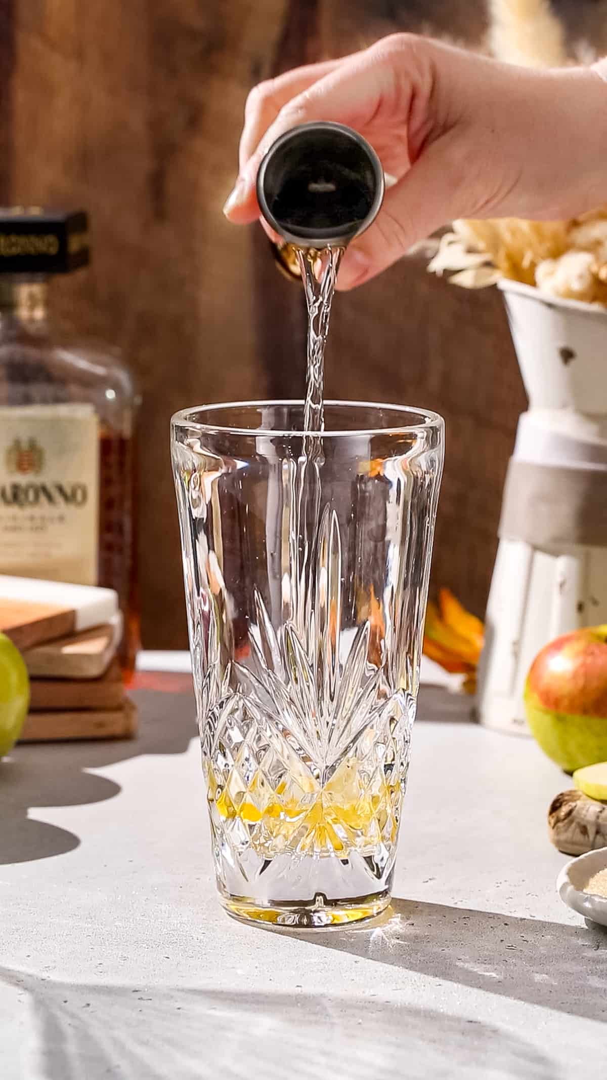 Hand pouring vodka into a cocktail shaker.