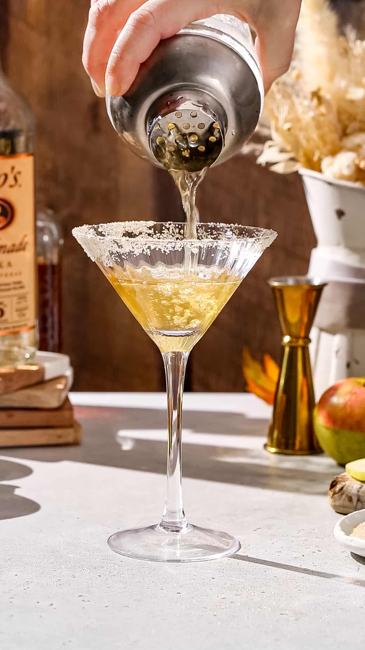 Hand straining a cocktail into a cocktail glass with a cinnamon sugar rim.