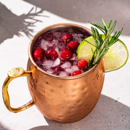 Overhead view of a Christmas Mule cocktail in a copper mug on a countertop. The drink is garnished with fresh cranberries, rosemary and a lime slice.