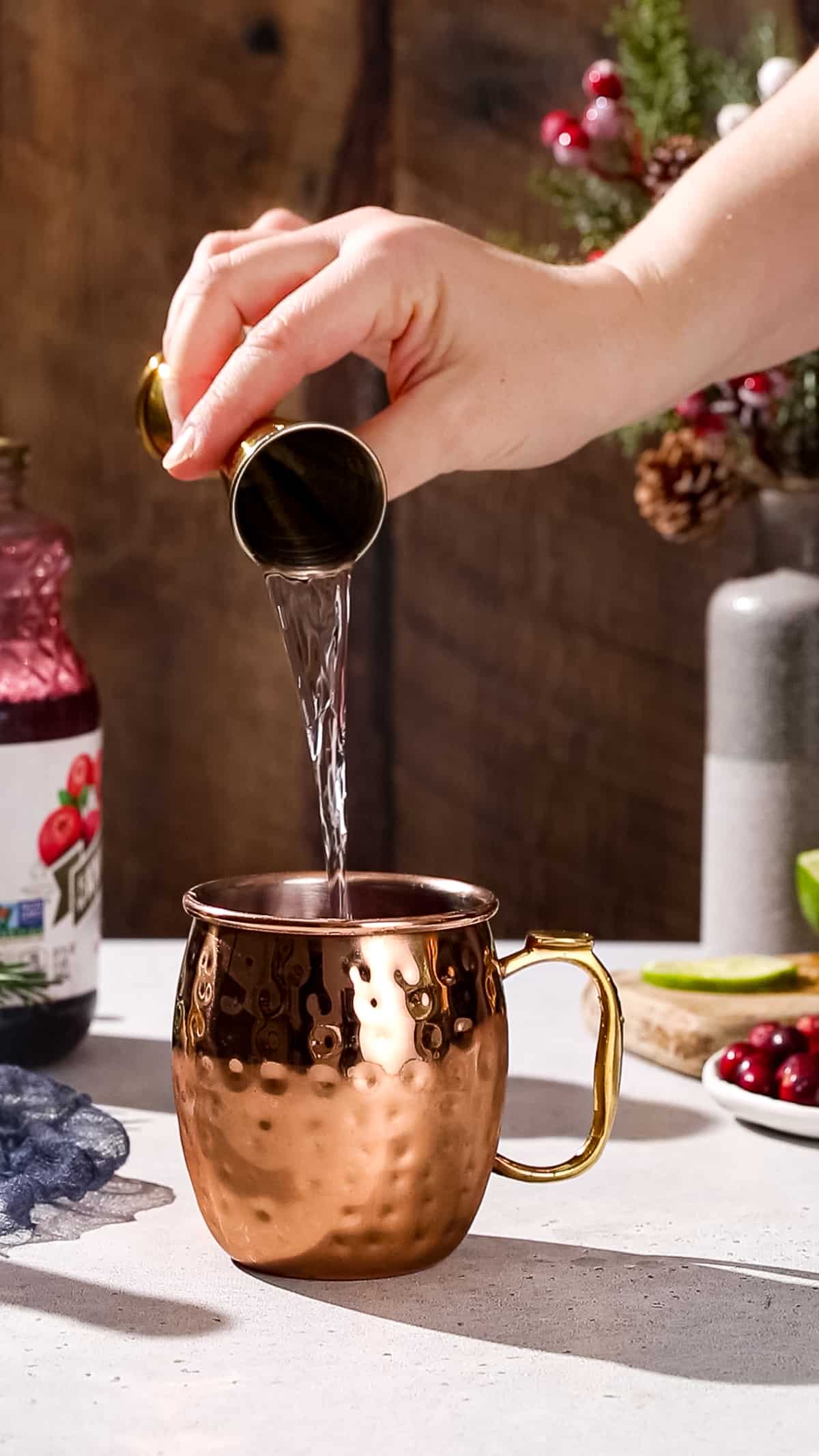 Hand pouring vodka into a copper mug.