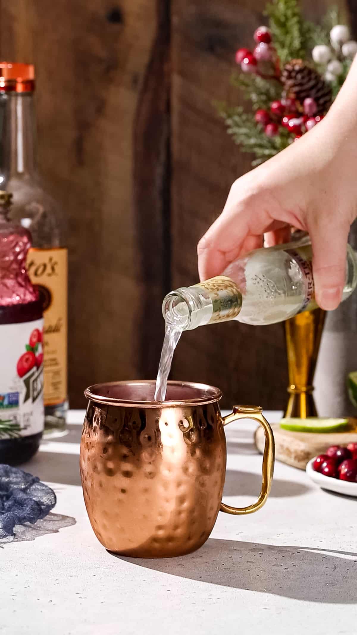 Hand pouring ginger beer from a glass bottle into a copper mug.