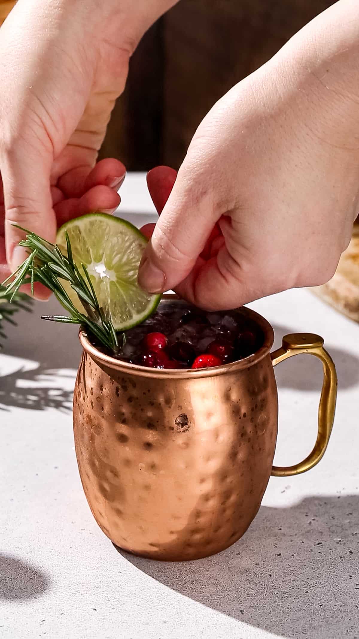 Hand adding a slice of lime to the rim of a copper mug.