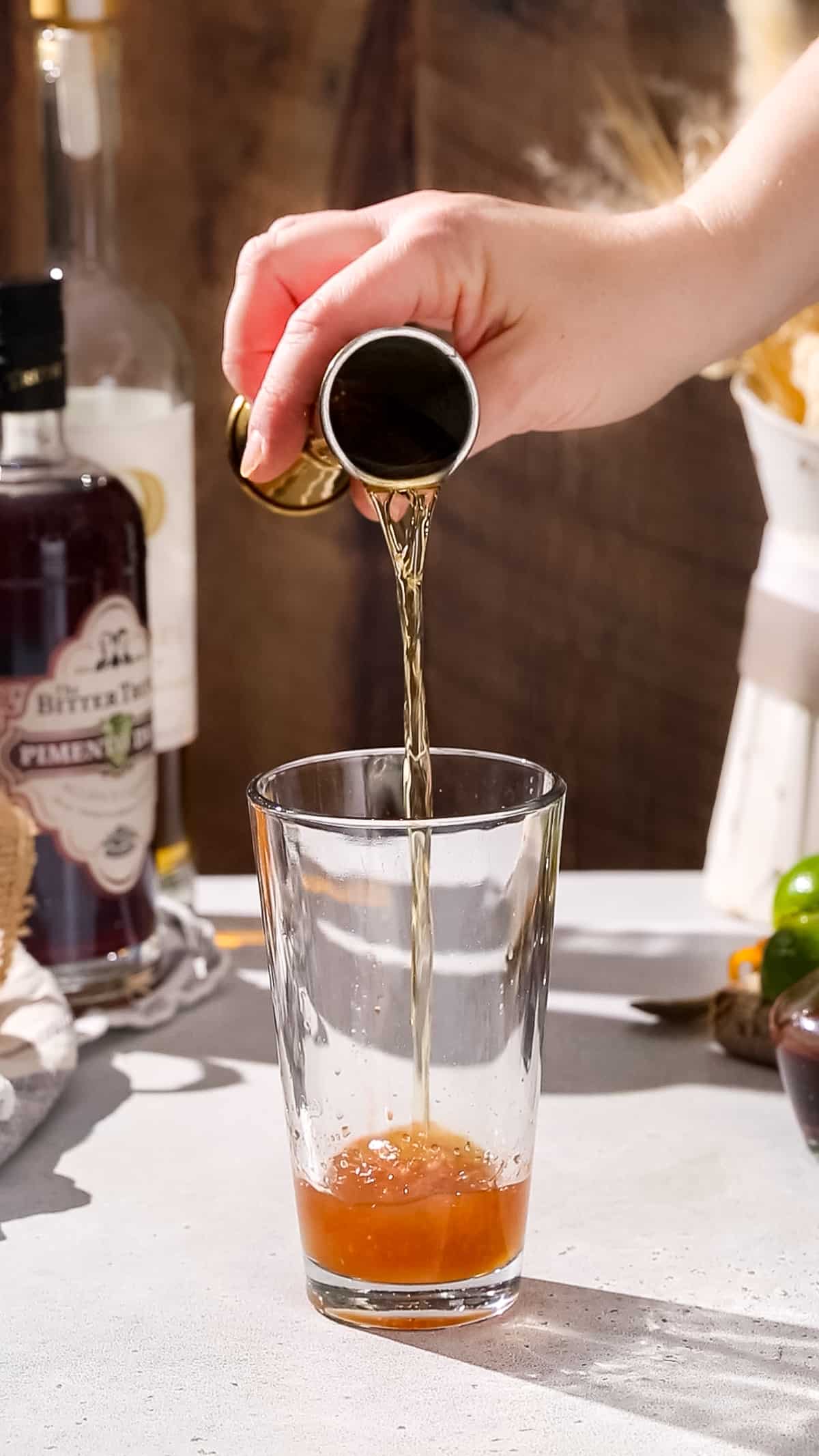 Hand adding bourbon to a cocktail shaker.