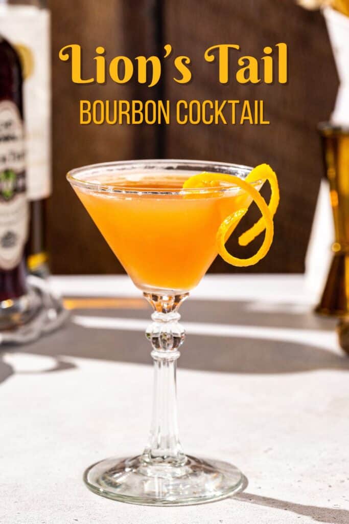 Lion’s Tail cocktail in a martini glass on a countertop. The drink is orange in color and has a long curly strip of orange peel as the garnish. In the background are ingredients and bar tools, and a text overlay above the drink says “Lion’s Tail bourbon cocktail”.