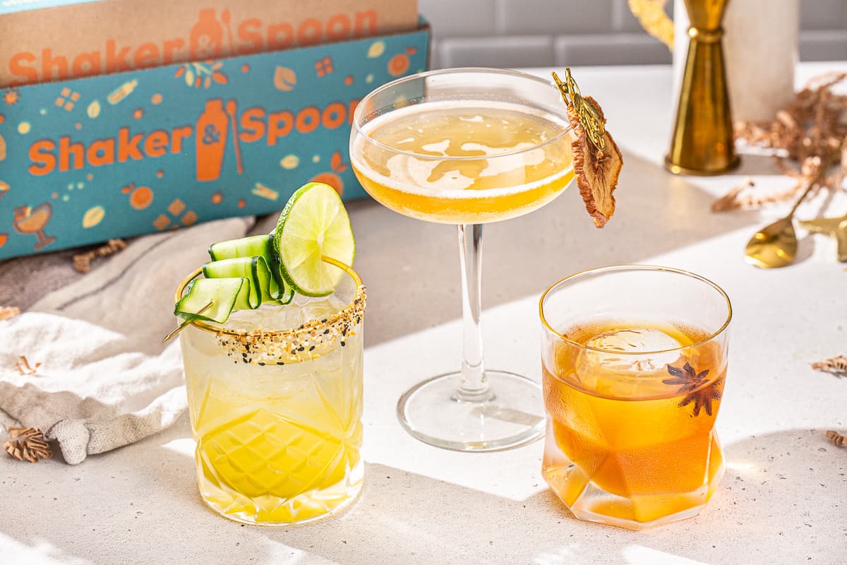 Three cocktails on a countertop with the Shaker & Spoon box in the background. These are the three cocktails you can make from the Shaker & Spoon vodka brunch box. Two are in old fashioned glasses and one is in a stemmed coupe glass.