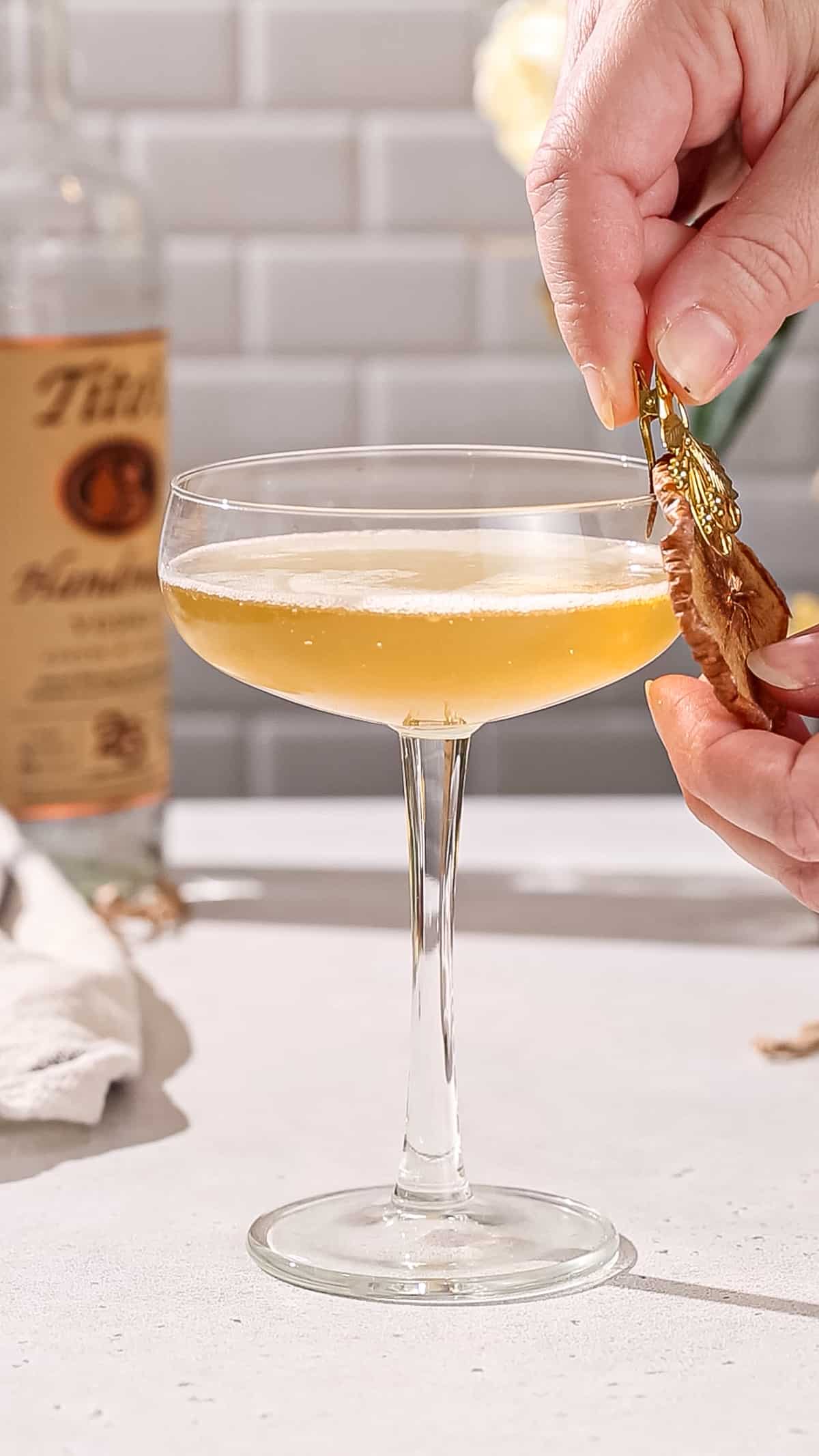 Dried apple garnish being clipped onto the rim of a cocktail glass.