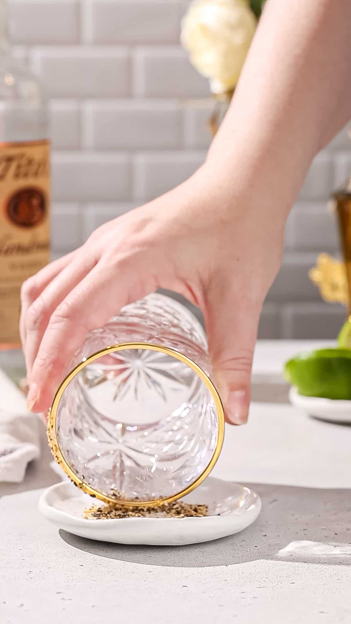 Hand dipping the wet rim of a cockail glass into a dish of seasoning.