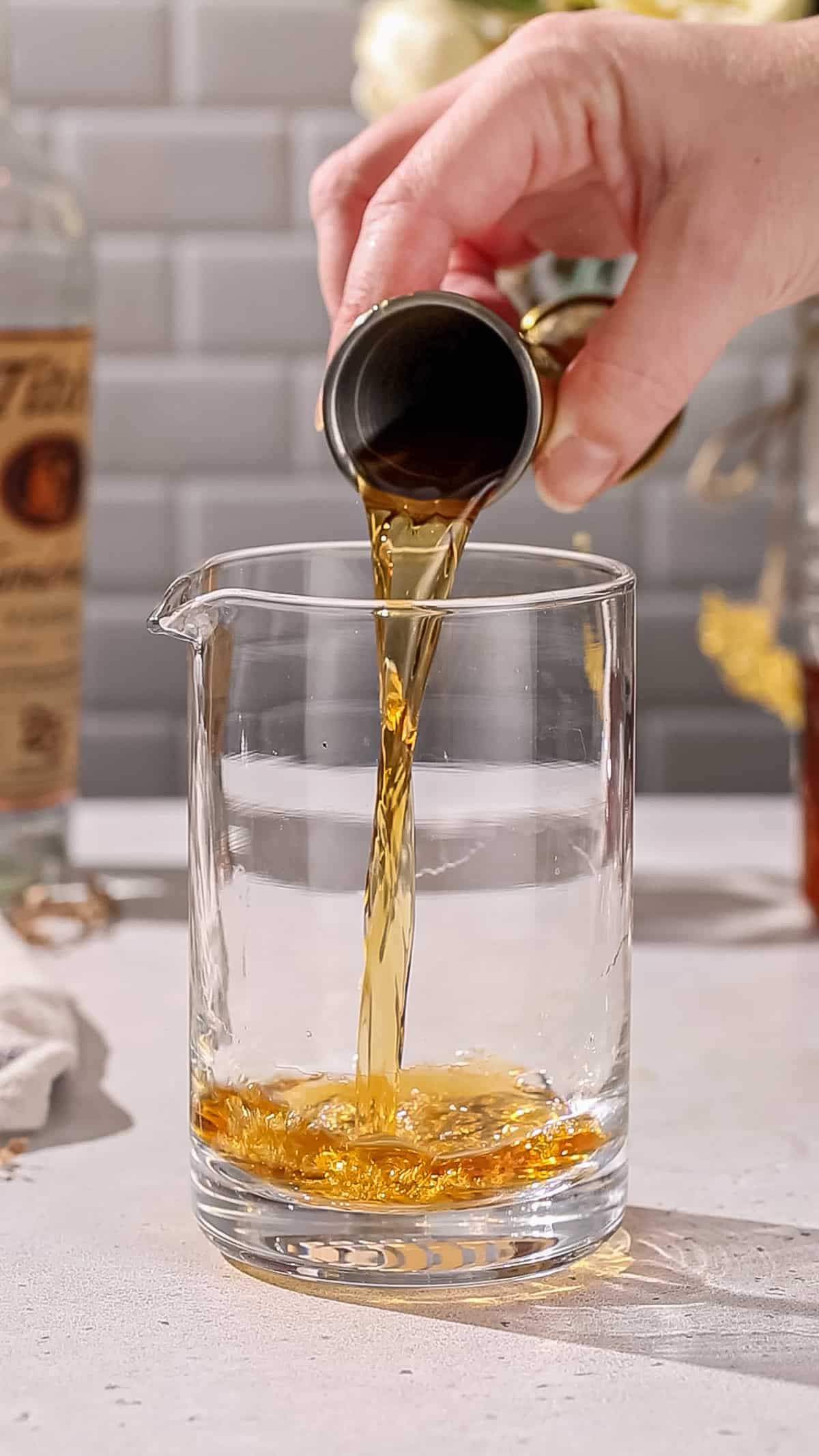Hand pouring tea-infused vodka into a cocktail mixing glass.