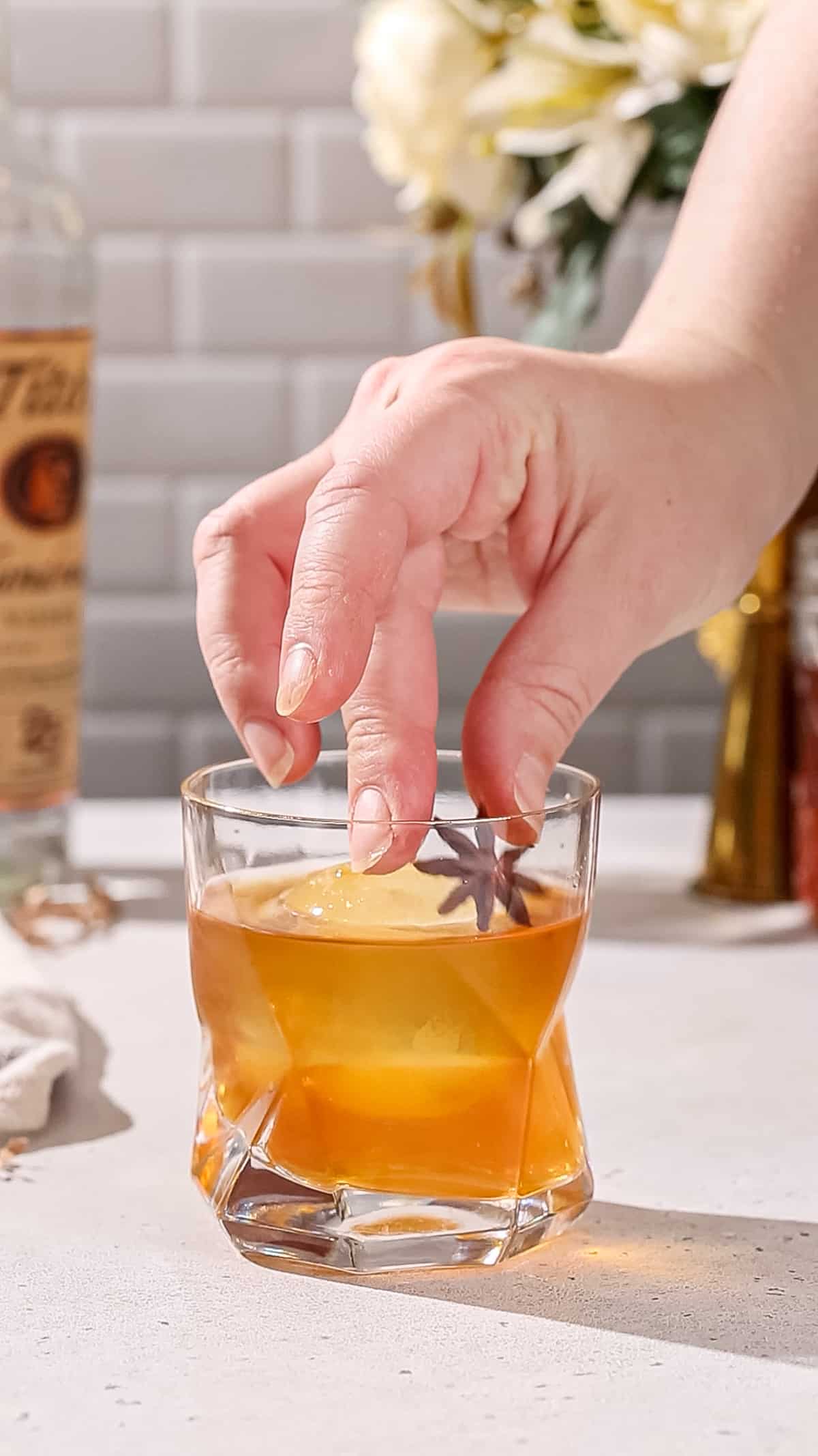 Hand adding a star anise as garnish to a cocktail.