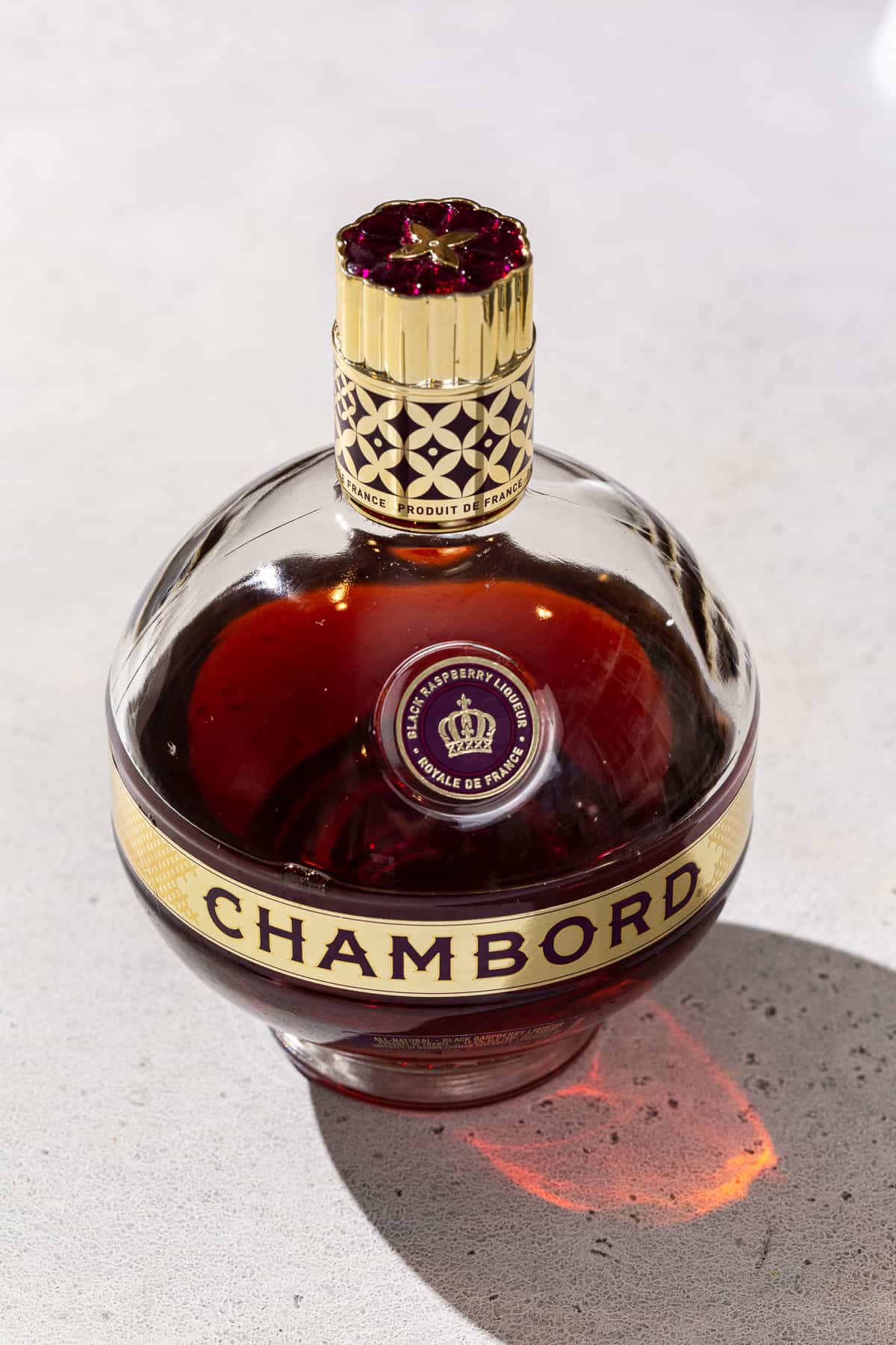 A bottle of Chambord liqueur on a countertop. The bottle has a distinctive round shape with a gold band around the middle and a gold screw top cap.