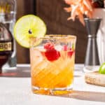 Side view of a Chambord Margarita cocktail on a countertop. The drink has a lime slice and fresh raspberry garnish. In the background, a bottle of Chambord can be seen off to the left.