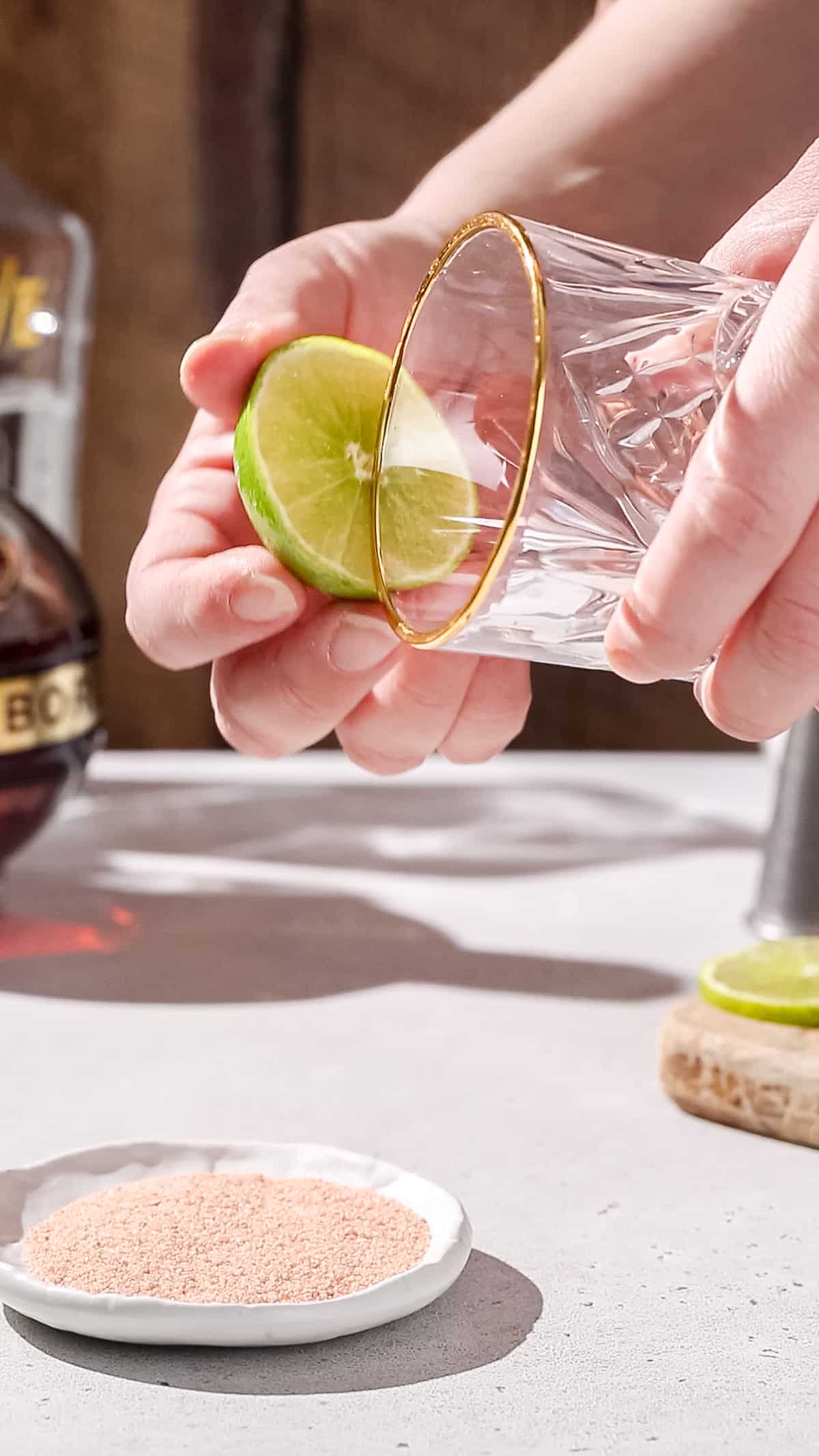 Hands using a cut lime to wet the rim of a cocktail glass.