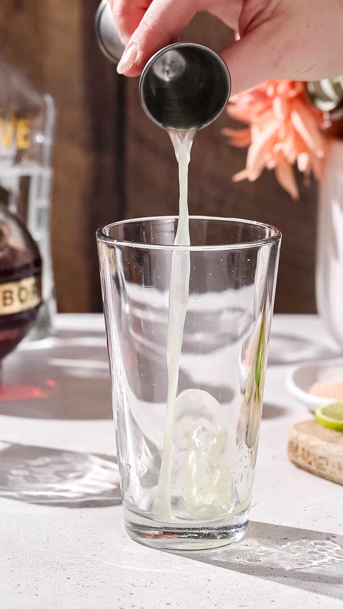 Hand using a jigger to add lime juice into a cocktail shaker.