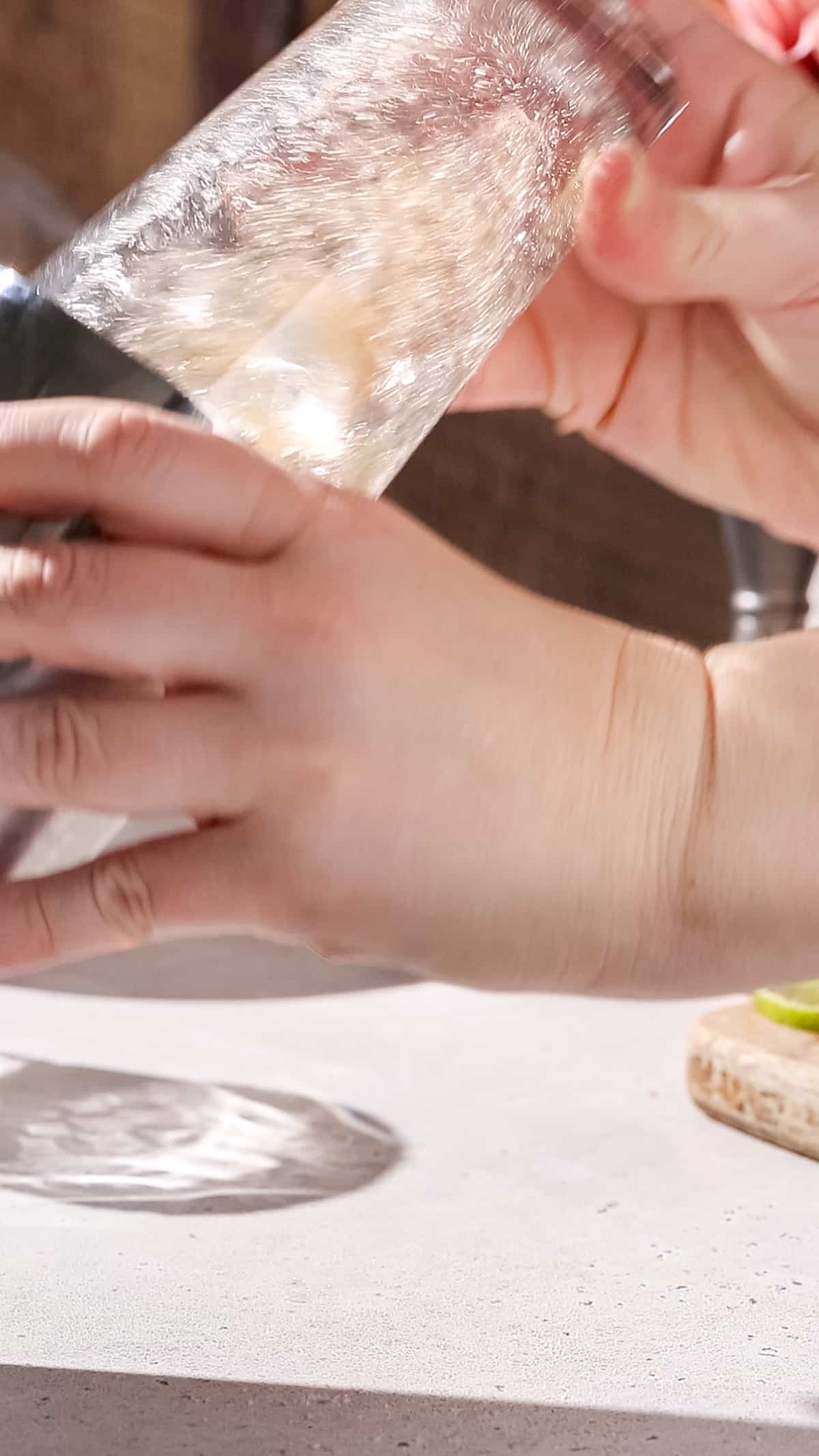 Hands shaking up a cocktail in a glass and metal shaker.