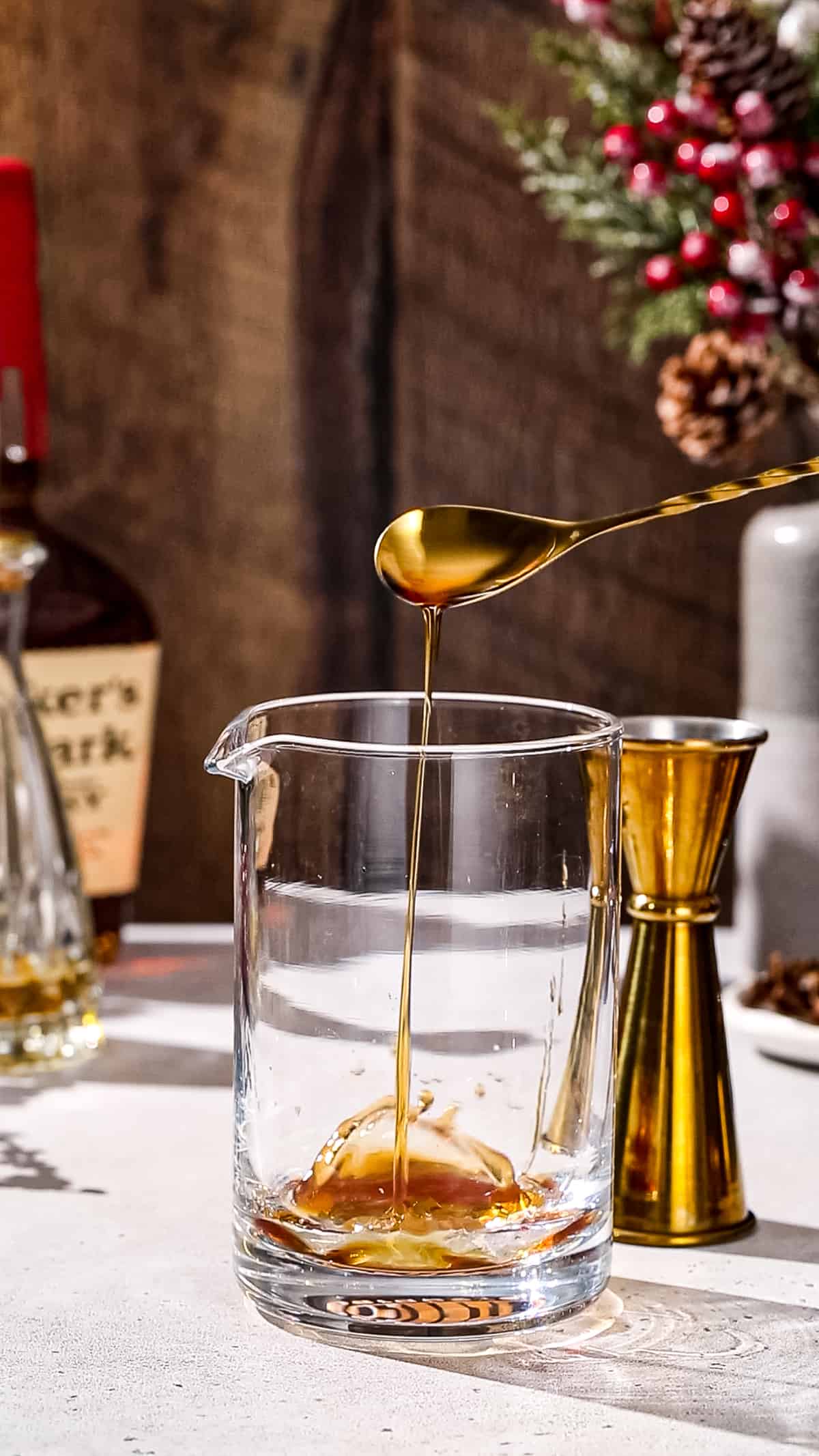 Cinnamon syrup being added to a cocktail mixing glass using a gold bar spoon.