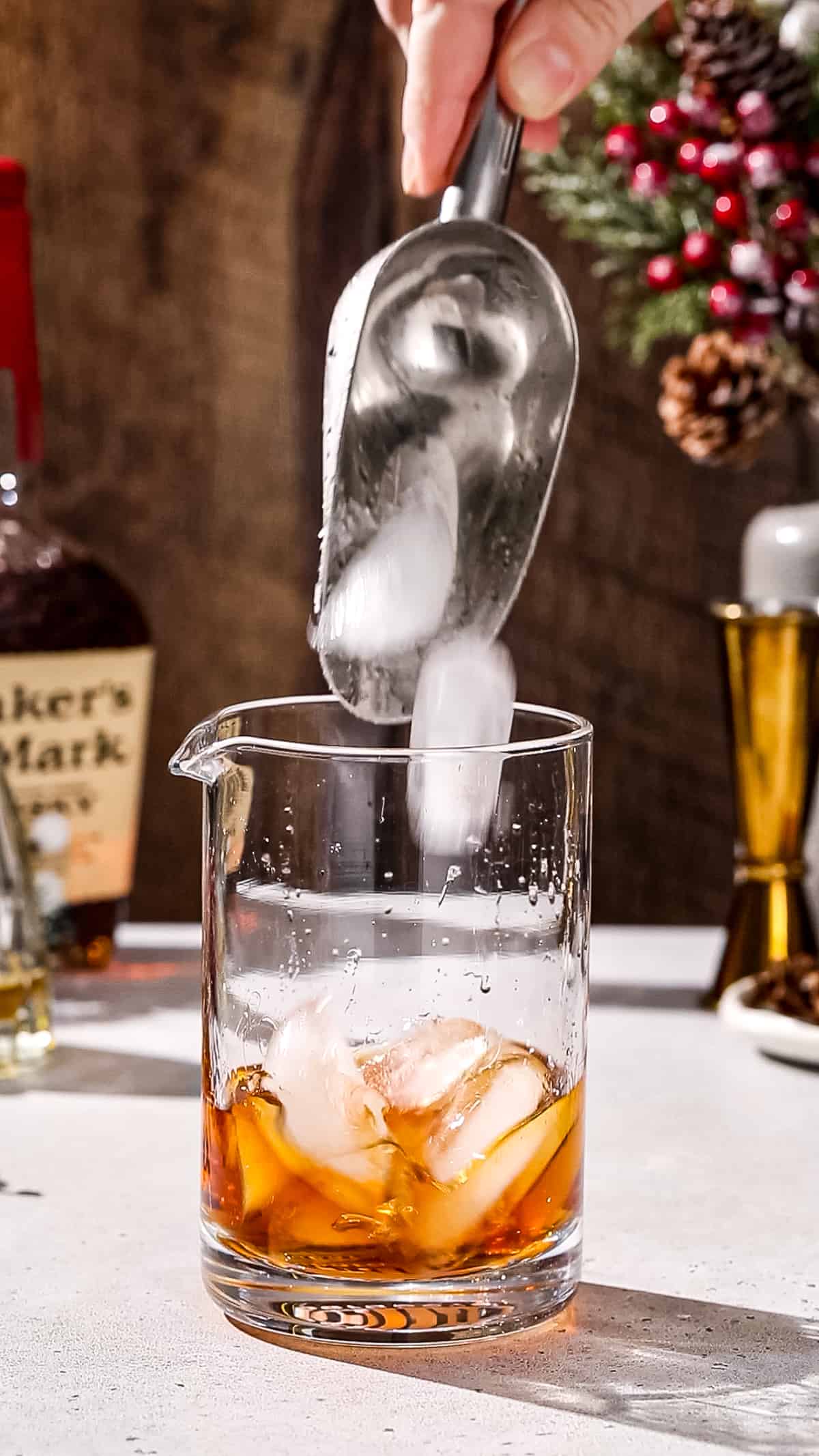 Hand using an ice scoop to add ice to a cocktail mixing glass.