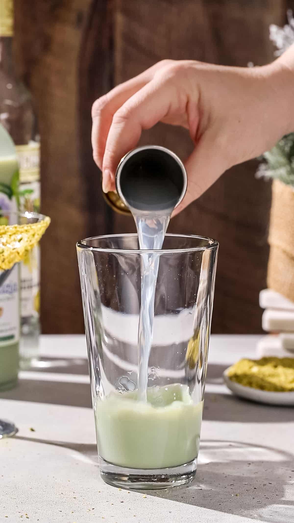 Hand adding vanilla vodka to a cocktail shaker.