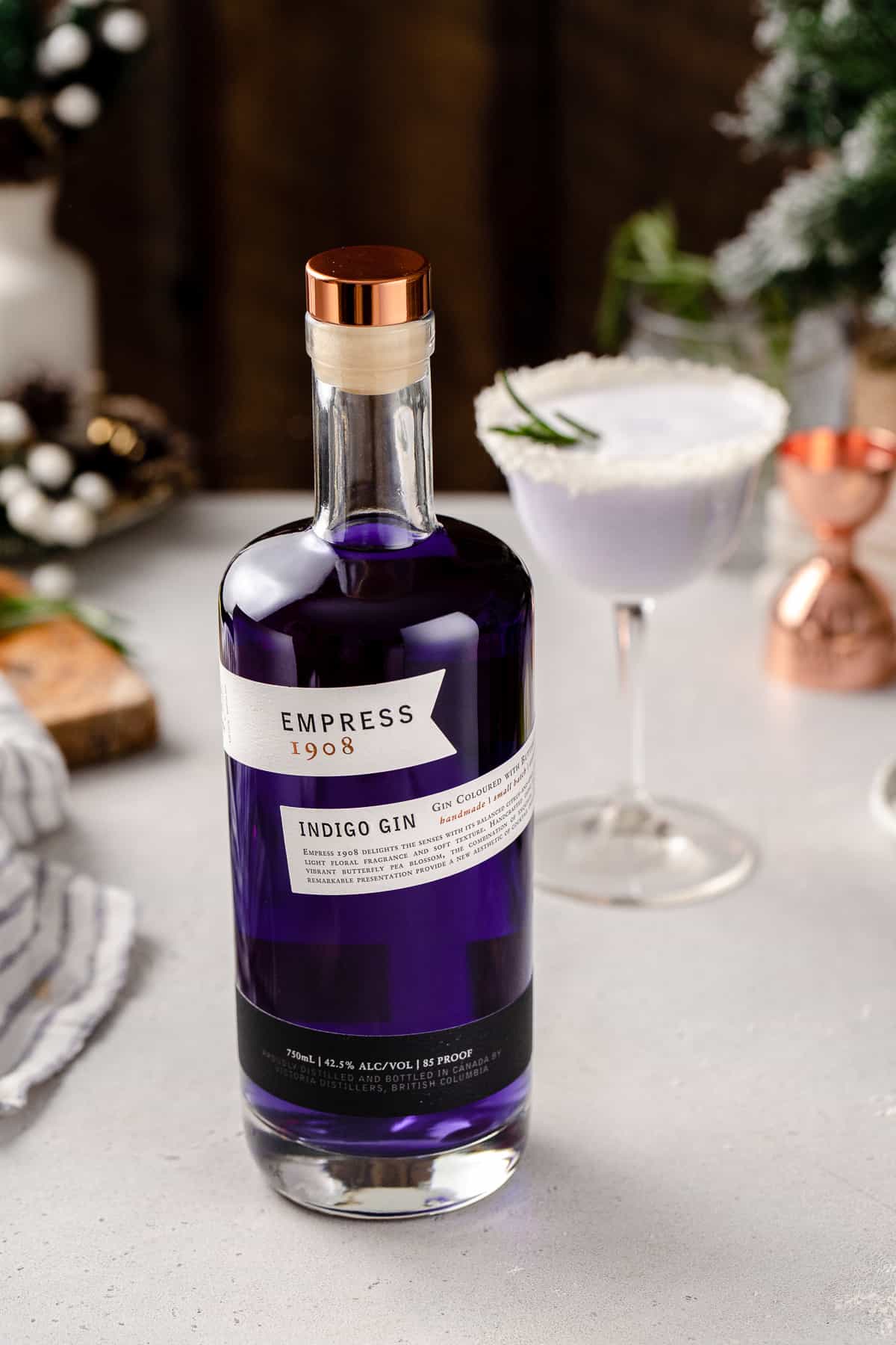 Empress Gin on a countertop with the Snowy Day cocktail in the background. Empress is an indigo-colored gin that uses butterfly pea flowers to get its distinctive color.