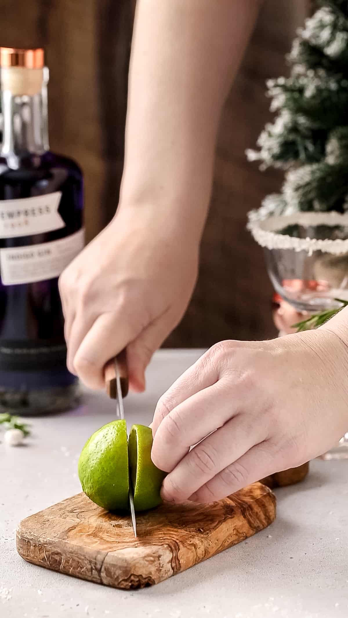 Hand using a knife to cut a lime in half.