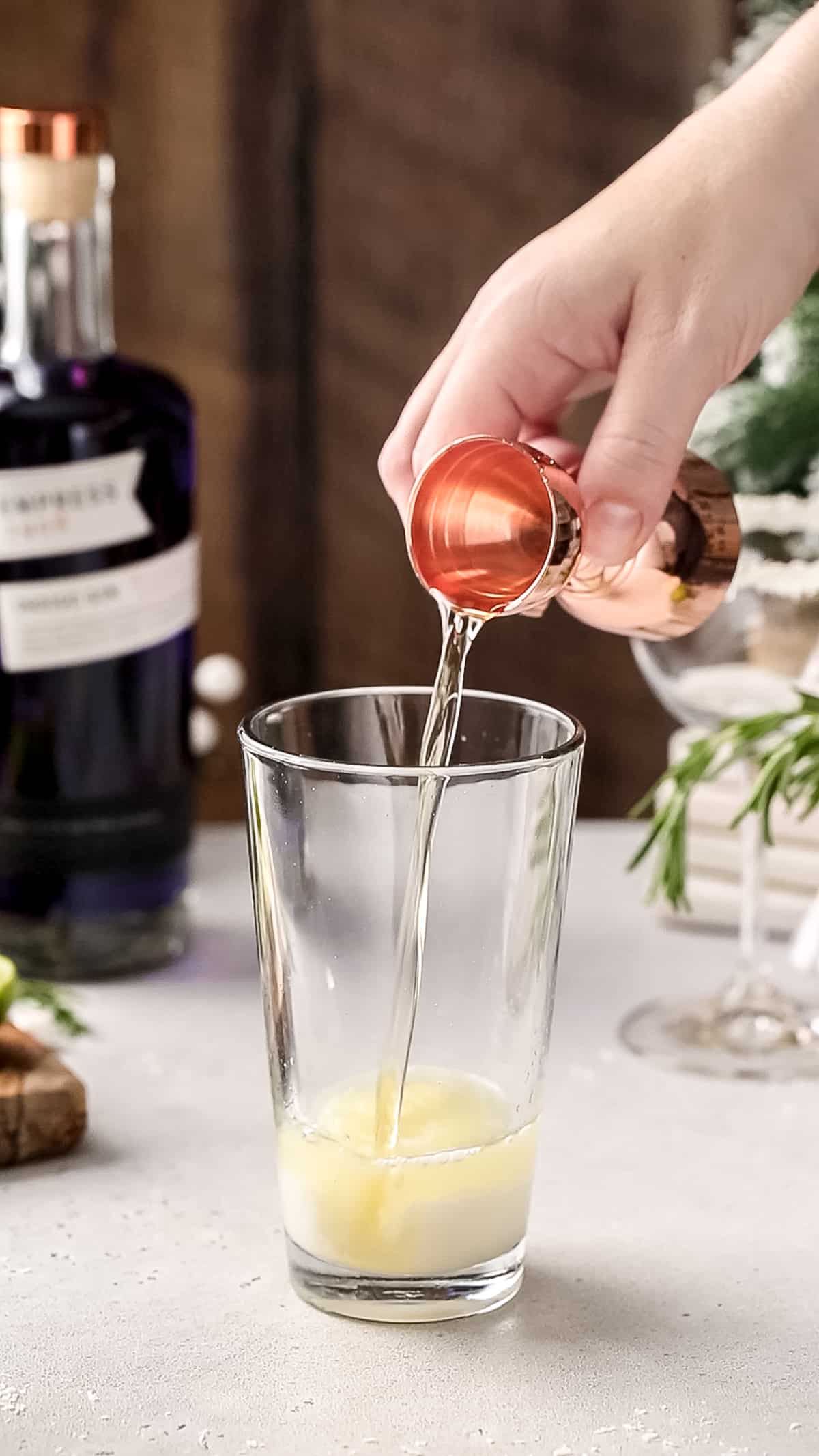 Hand adding golden falernum liqueur to a cocktail shaker.