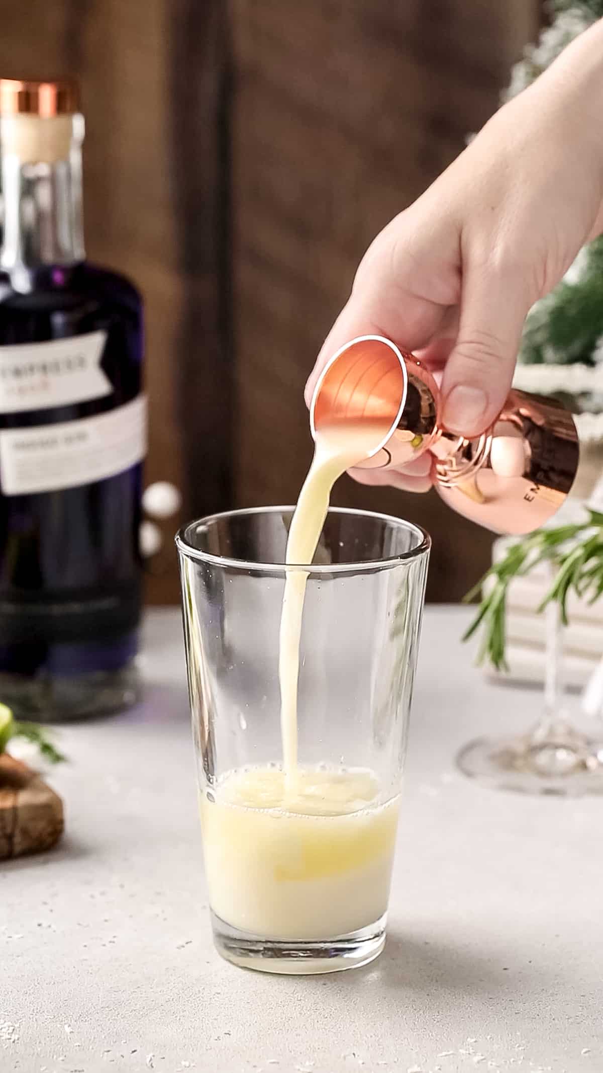 Hand adding pasteurized egg whites to a cocktail shaker.