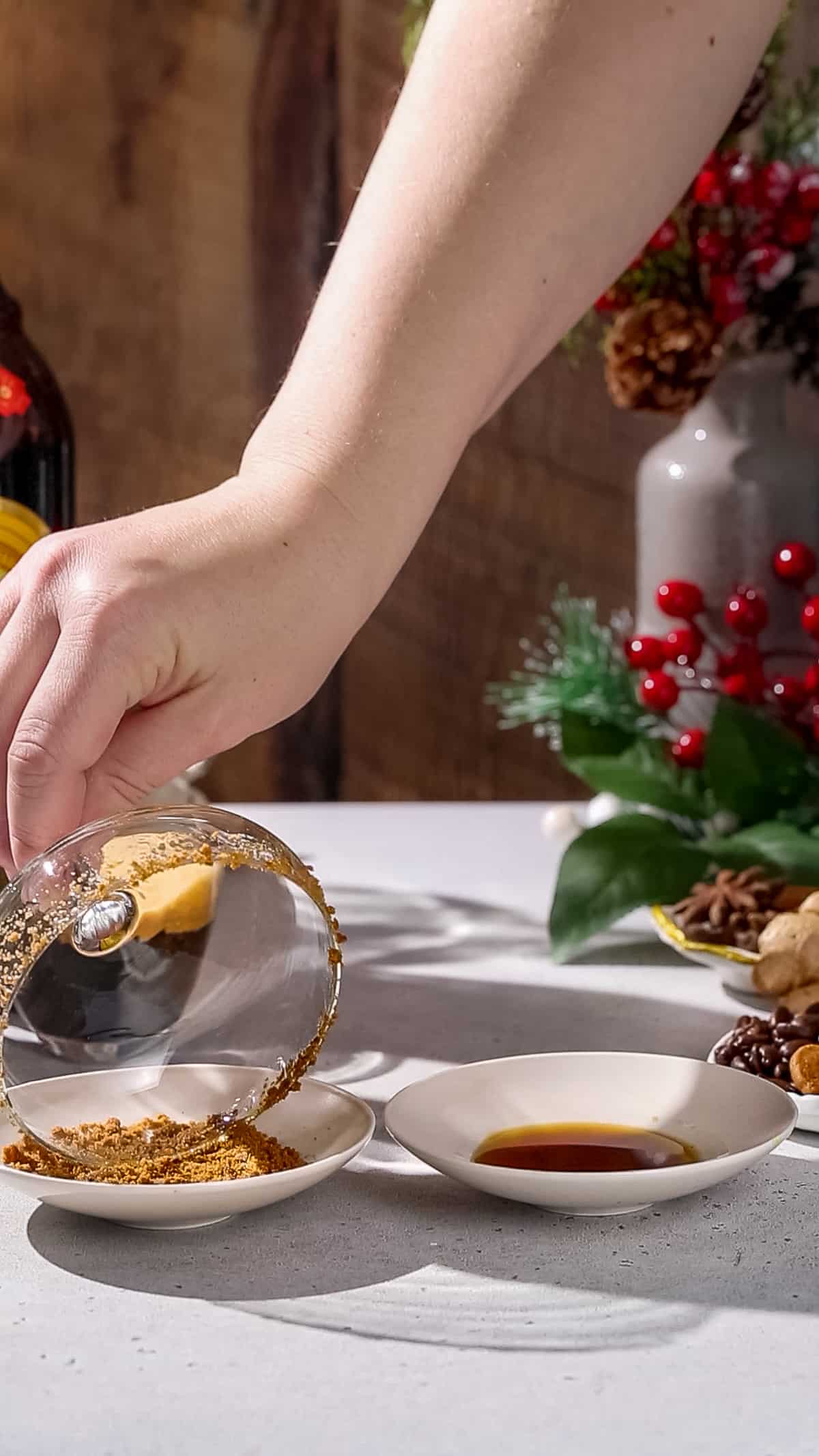 Hand dipping the rim of a cocktail glass into gingerbread cookie crumbs.