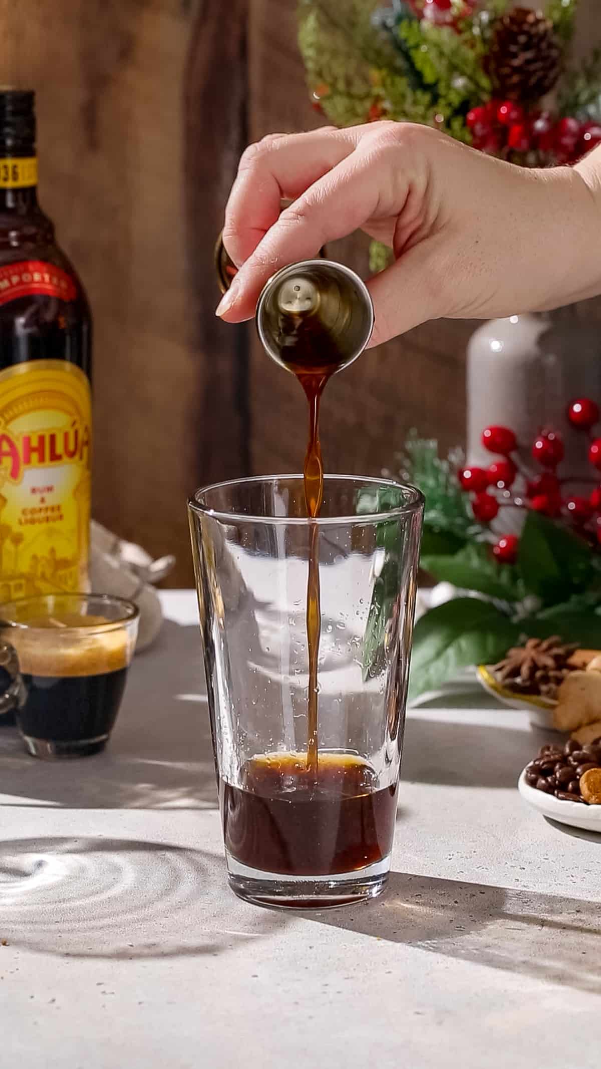 Hand using a jigger to add gingerbread syrup to a cocktail shaker.