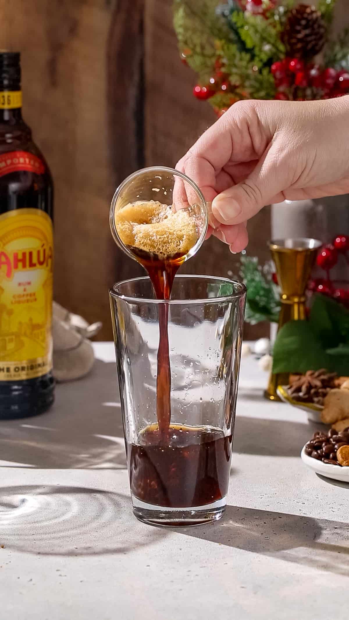 Hand adding espresso to a cocktail shaker.