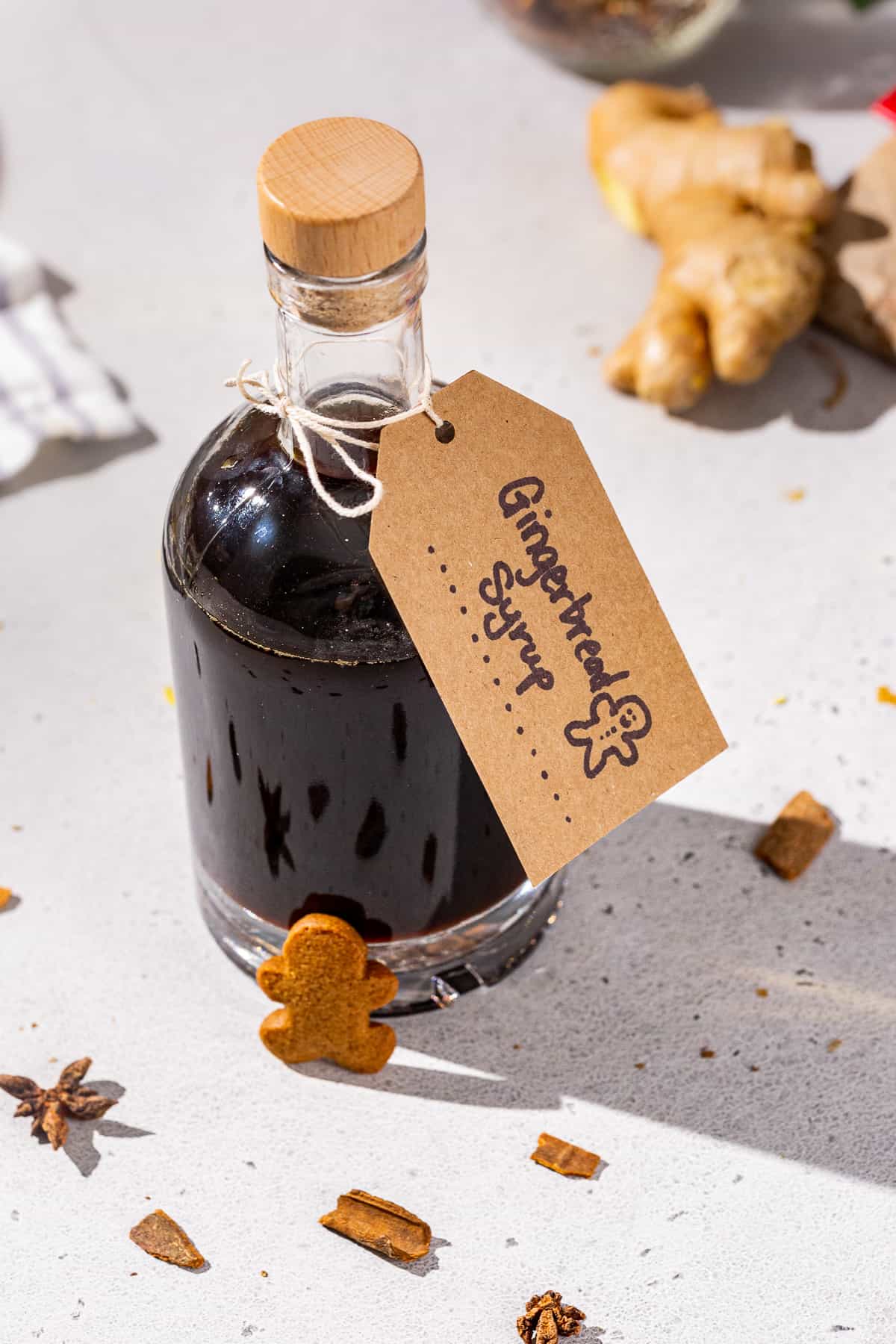 Overhead view of a bottle of Gingerbread syrup. The bottle has a little gingerbread man resting against it and some fresh ginger is seen in the background.