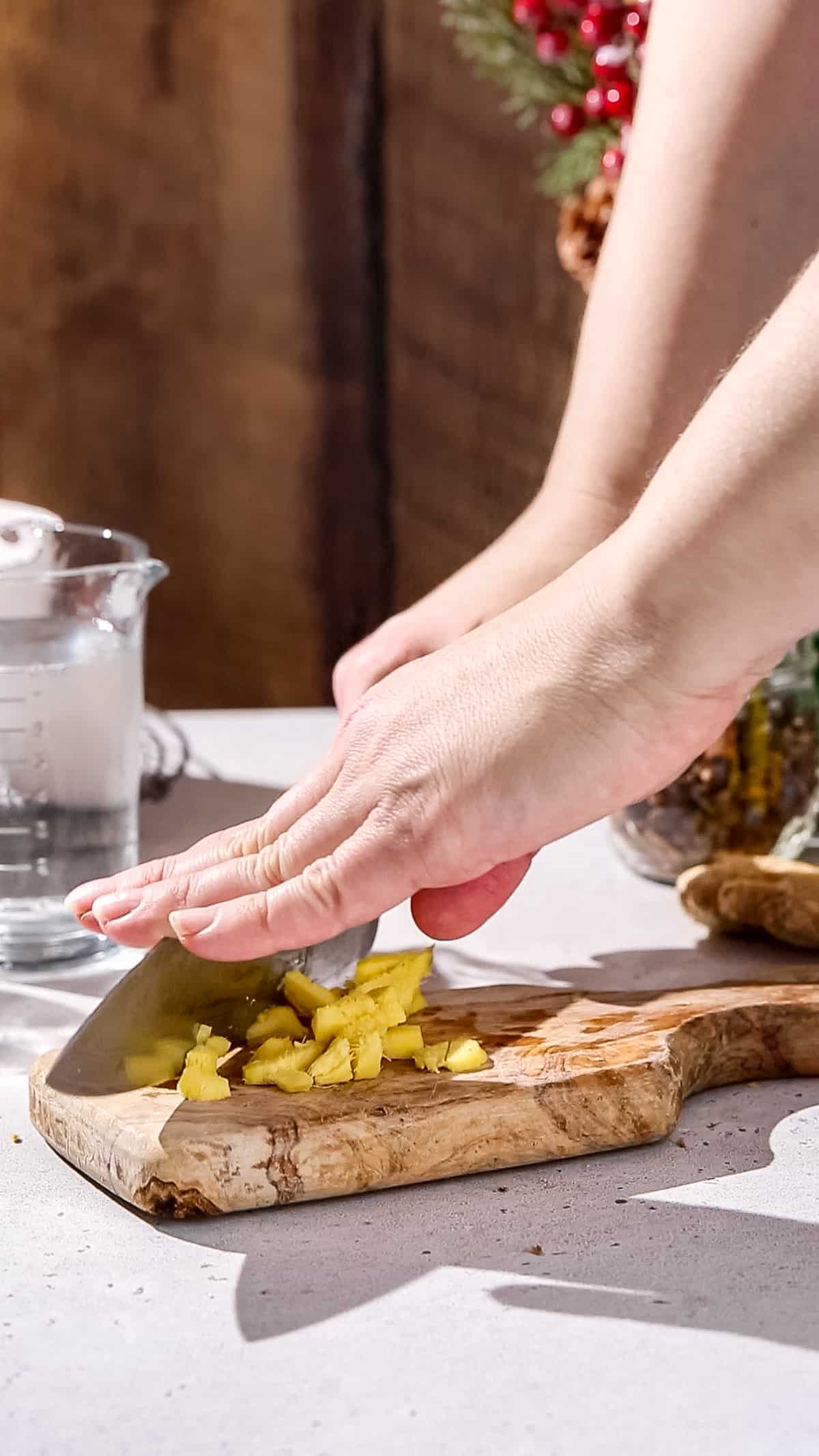 Hands using a knife to chop up fresh ginger.