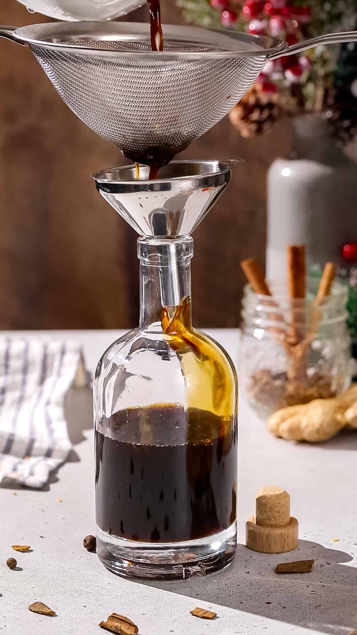 Straining gingerbread syrup through a fine mesh strainer and a funnel into a storage bottle.