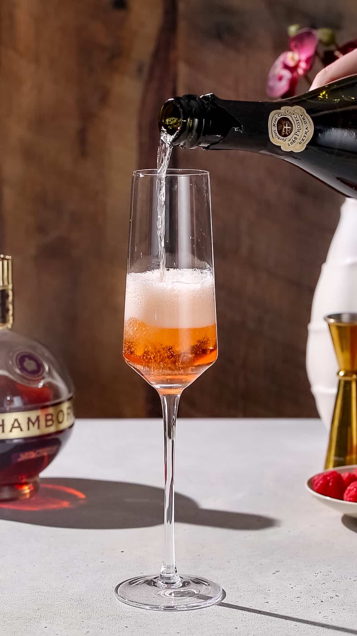 Hand pouring champagne into a champagne flute that also has chambord liqueur in it.