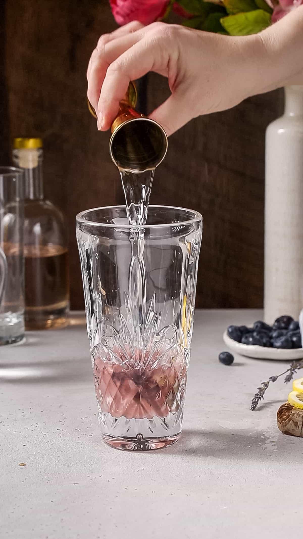 Hand pouring water into a cocktail shaker.