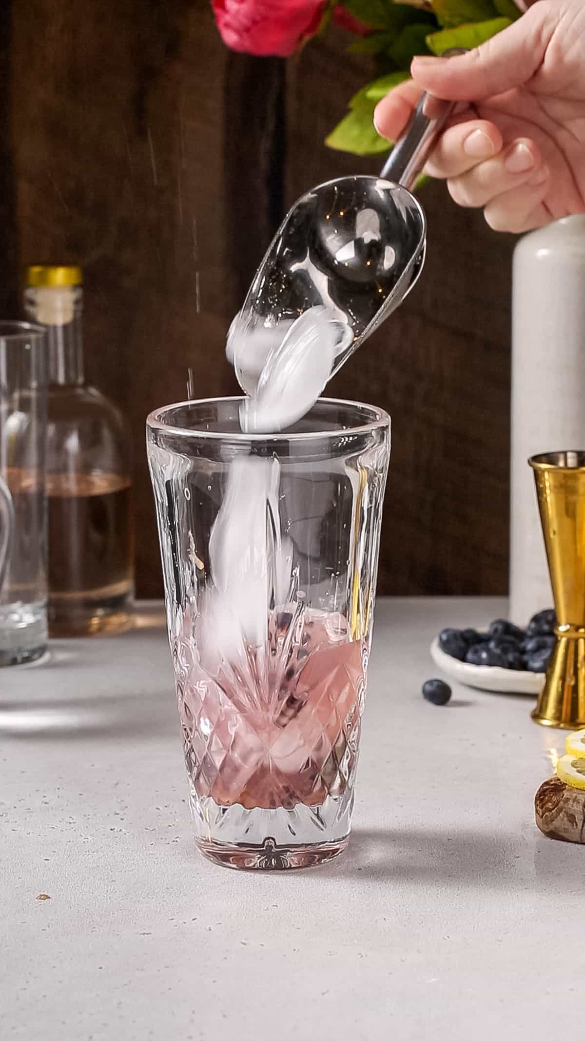 Hand using an ice scoop to add ice to a cocktail shaker.