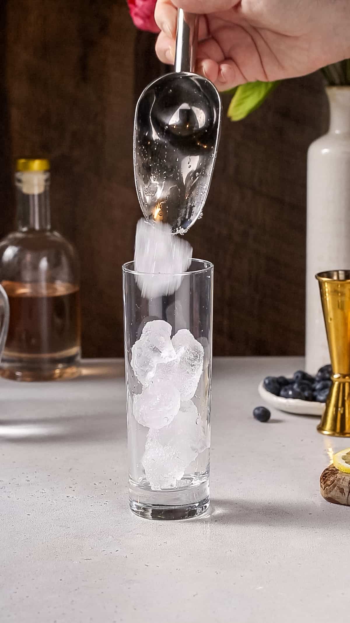 Hand using an ice scoop to fill a cocktail glass with ice.