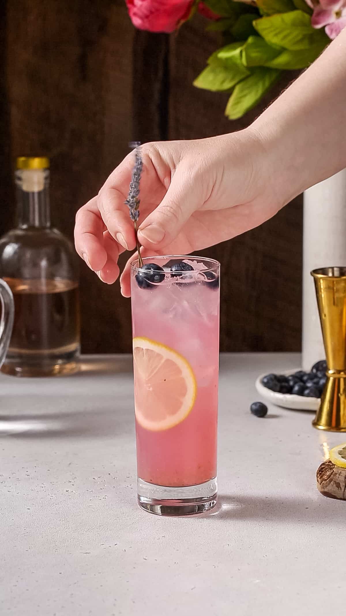 Hand adding a stalk of lavender flower to a pink drink.