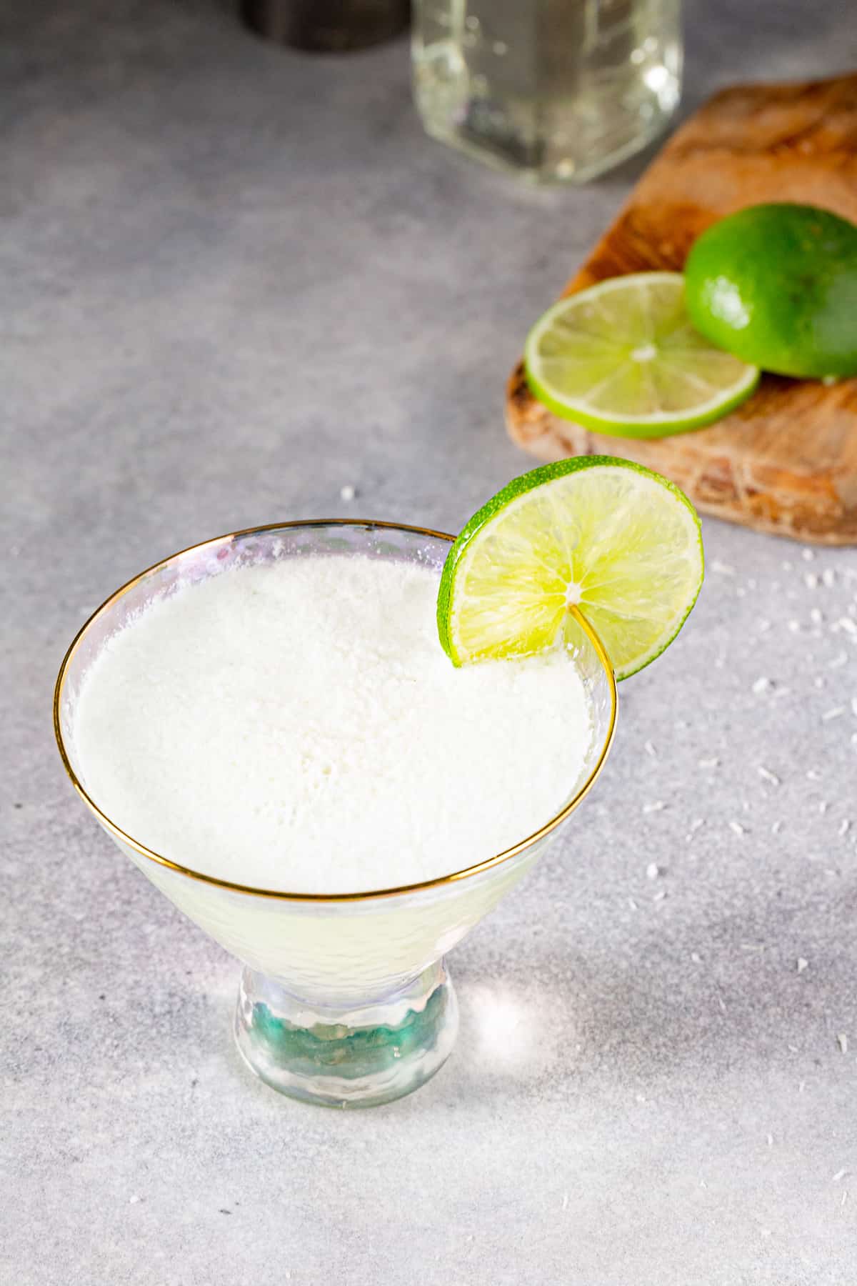 Overhead view of a lime mocktail with coconut milk. The non-alcoholic drink is in a martini glass and has a lime slice as garnish. A cut lime is seen in the background.