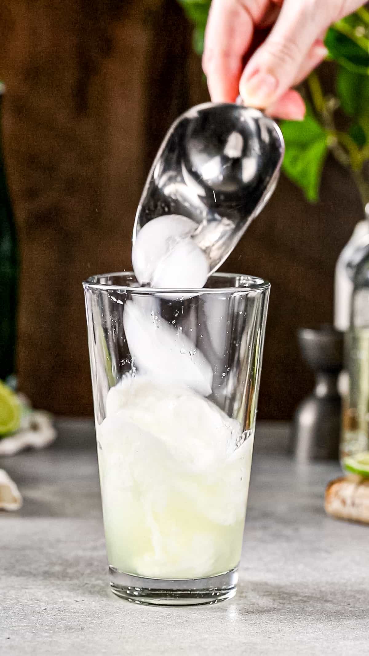 Hand adding ice to a cocktail shaker.