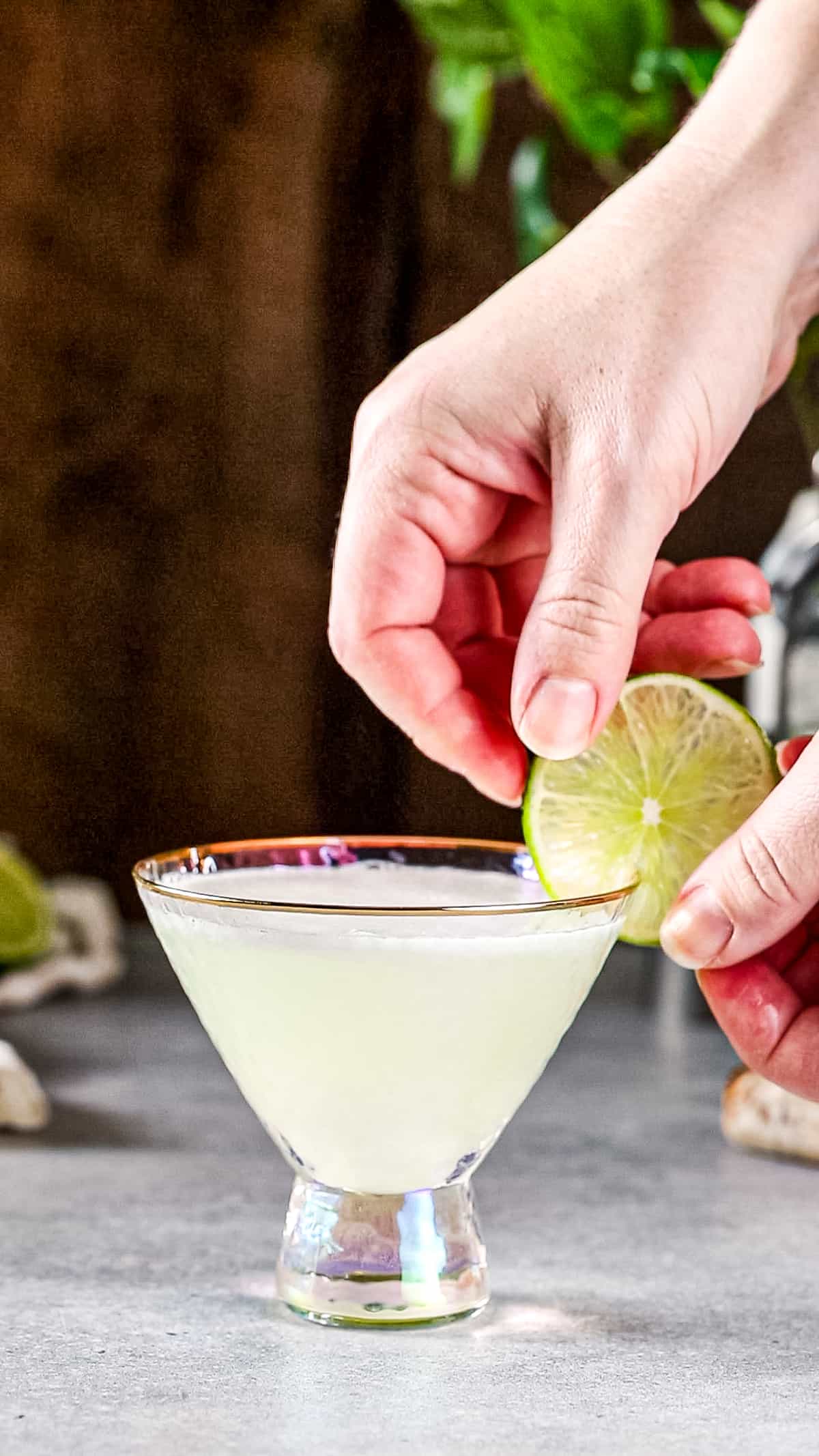 Hand adding a lime slice to the side of a martini glass.