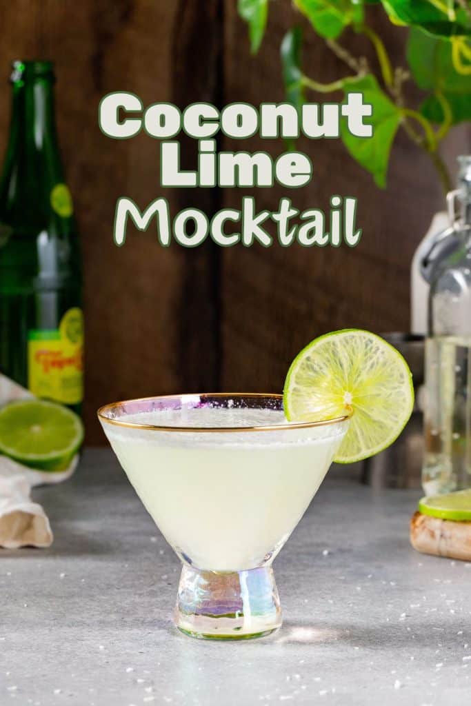 Coconut Lime Mocktail in a martini glass on a countertop. In the background are limes, some Topo Chico, a cutting board, a bottle of syrup and a jigger. Text overlay above the drink says “Coconut Lime Mocktail” in bold green lettering.