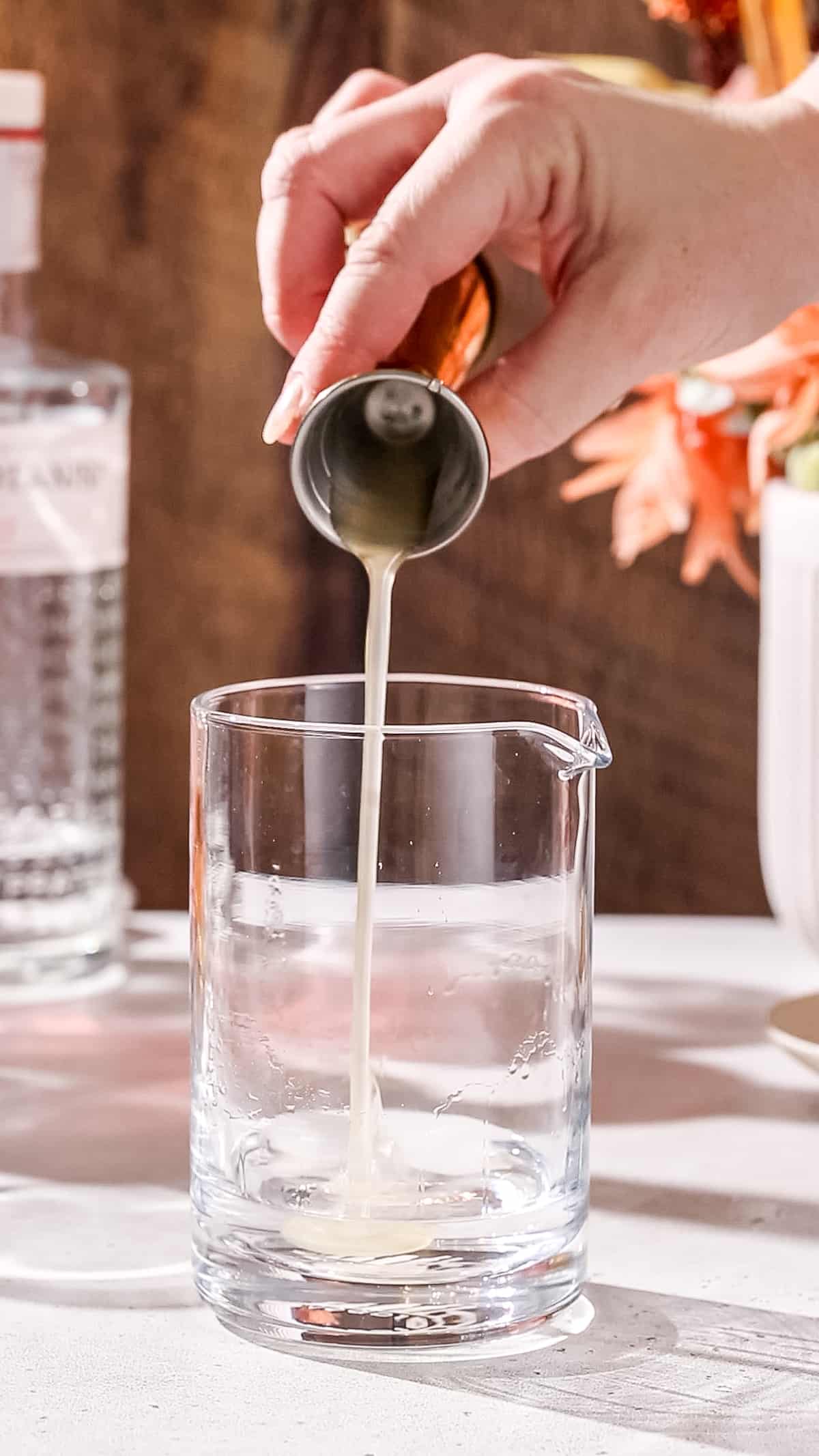 Hand pouring lychee puree syrup into a cocktail mixing glass.