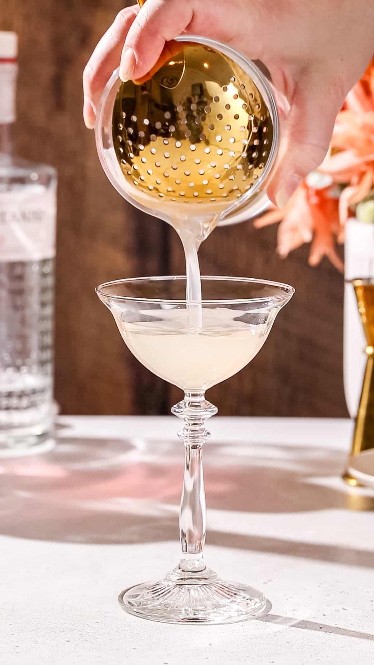 Hand straining a cocktail into a fancy coupe glass.