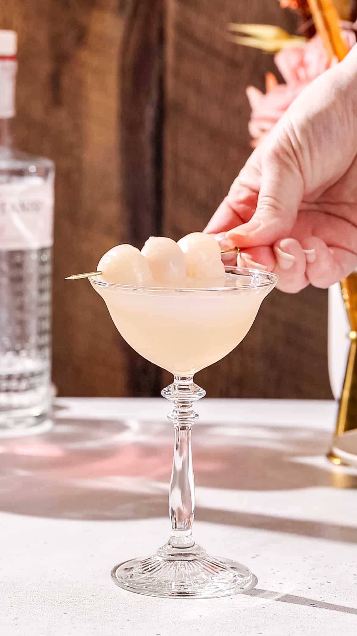 Hand adding a lychee fruit garnish to a cocktail.