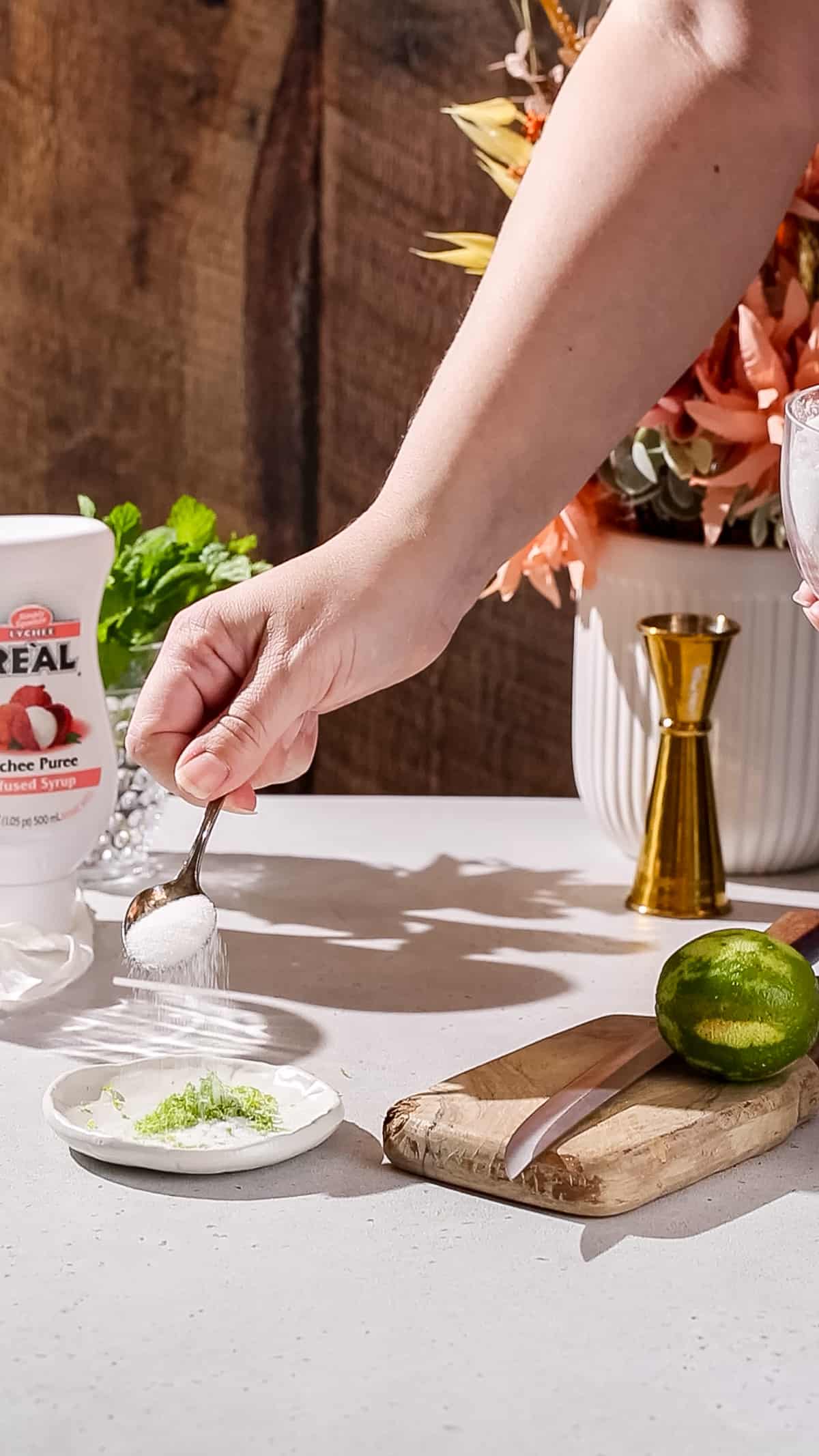 Hand putting sugar onto a dish of lime zest.