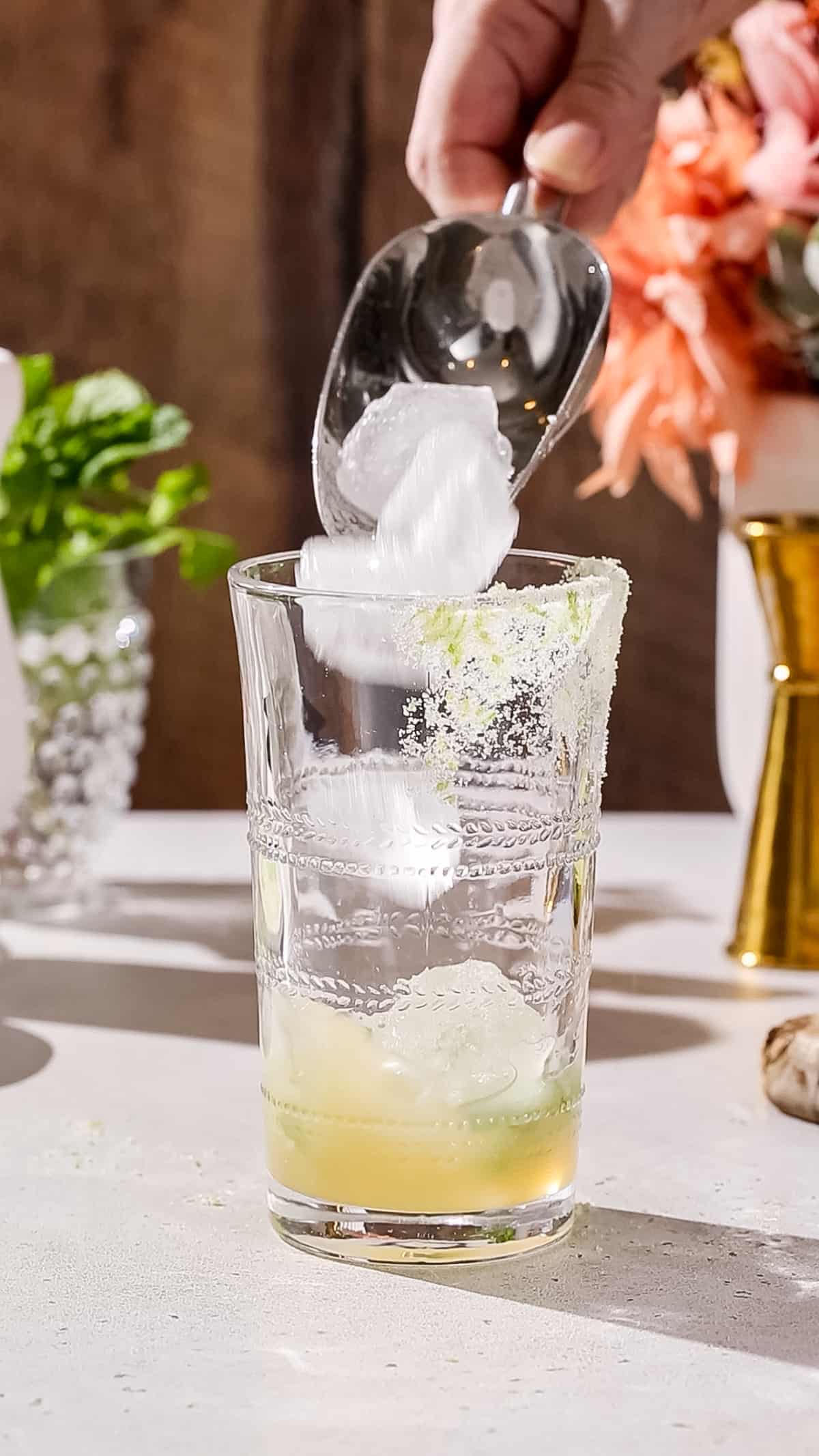 Hand using an ice scoop to add ice to a cocktail glass.